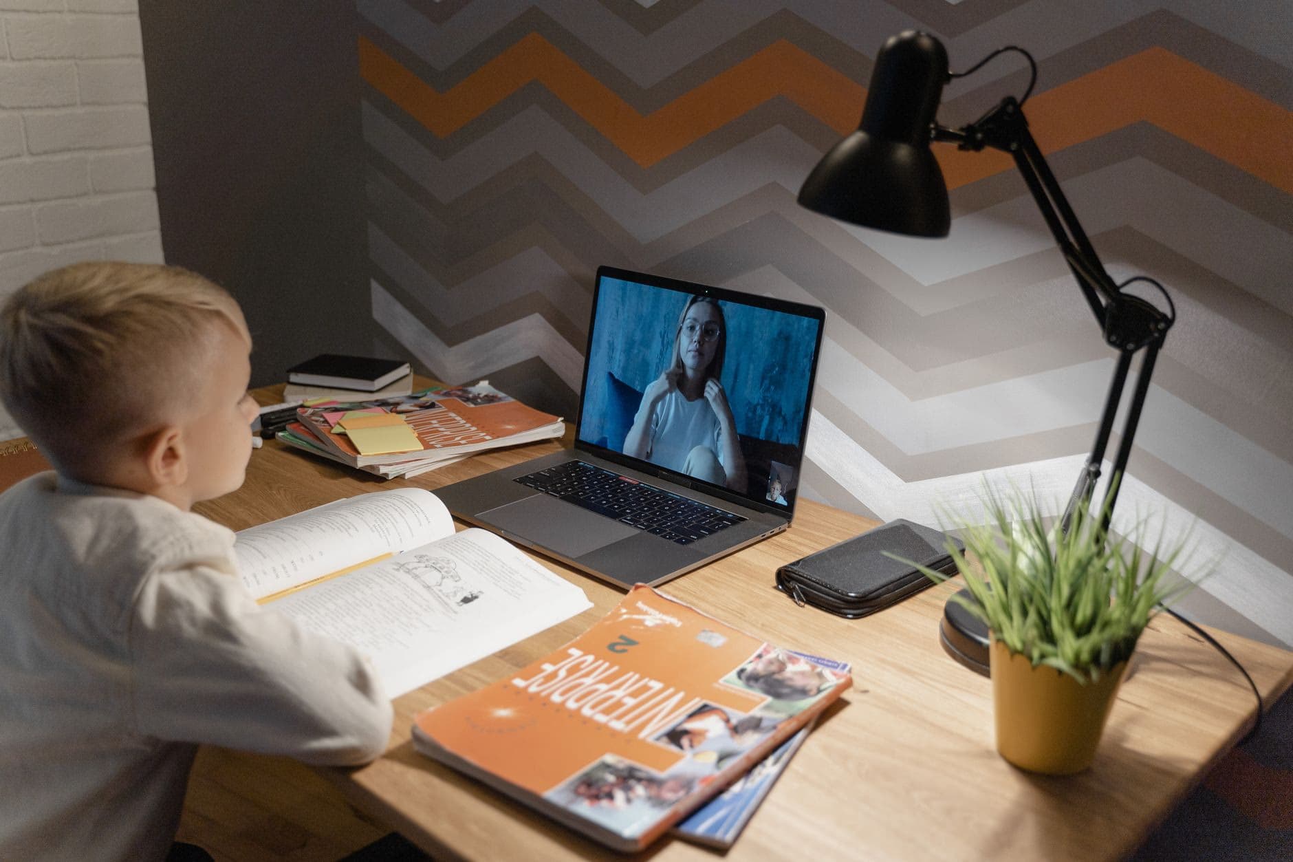 A student attending an online class on a laptop at a home desk