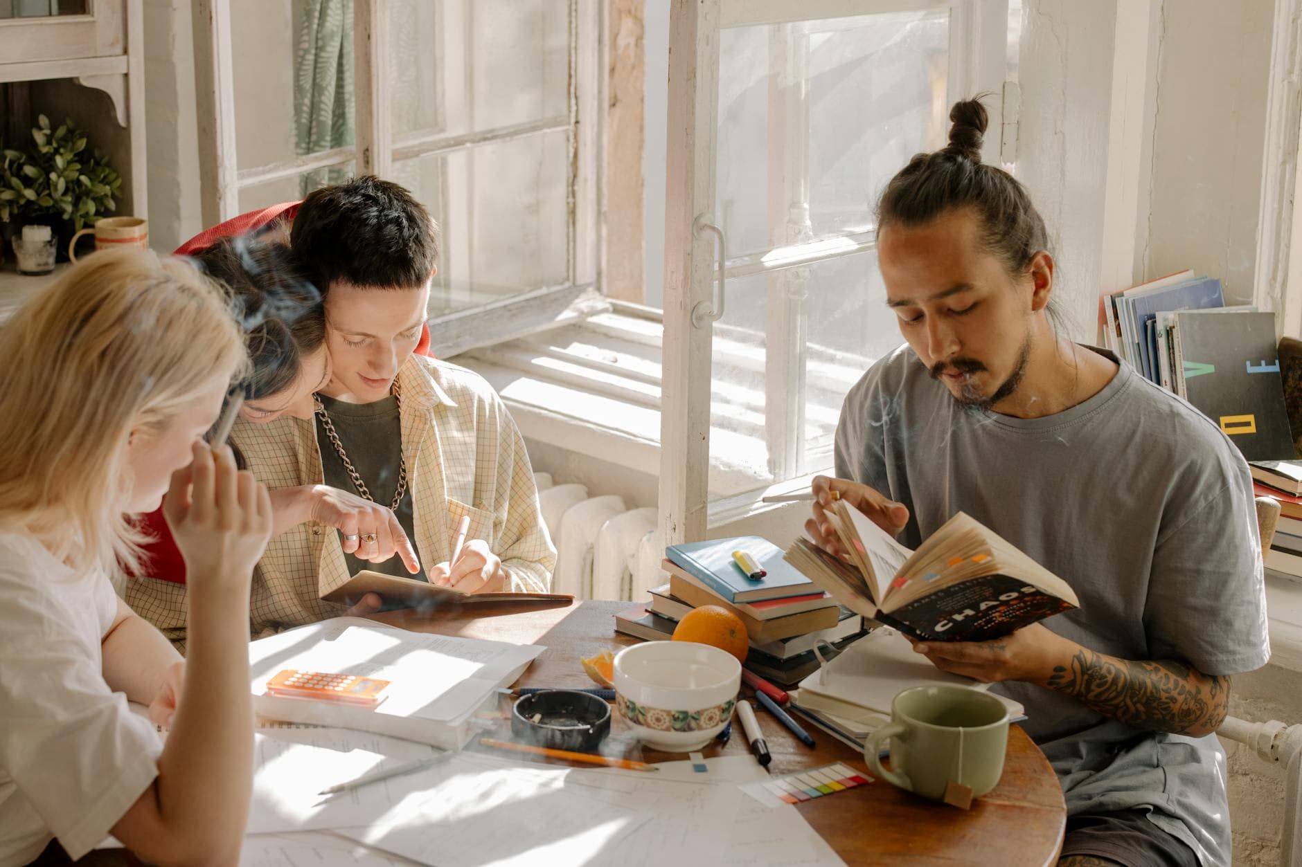 Group of college students collaborating and studying together on a sunny day in a dorm room.