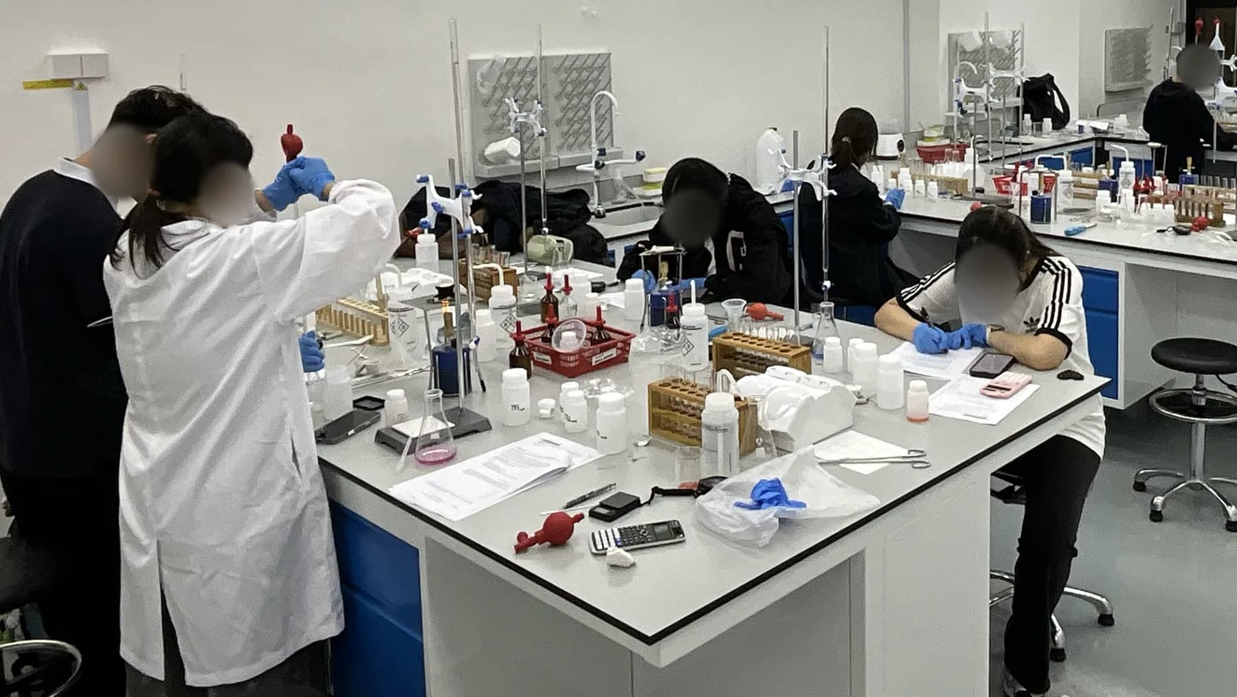 Students using a pipette and titration apparatus at shared laboratory benches during an Eclat Chemistry session