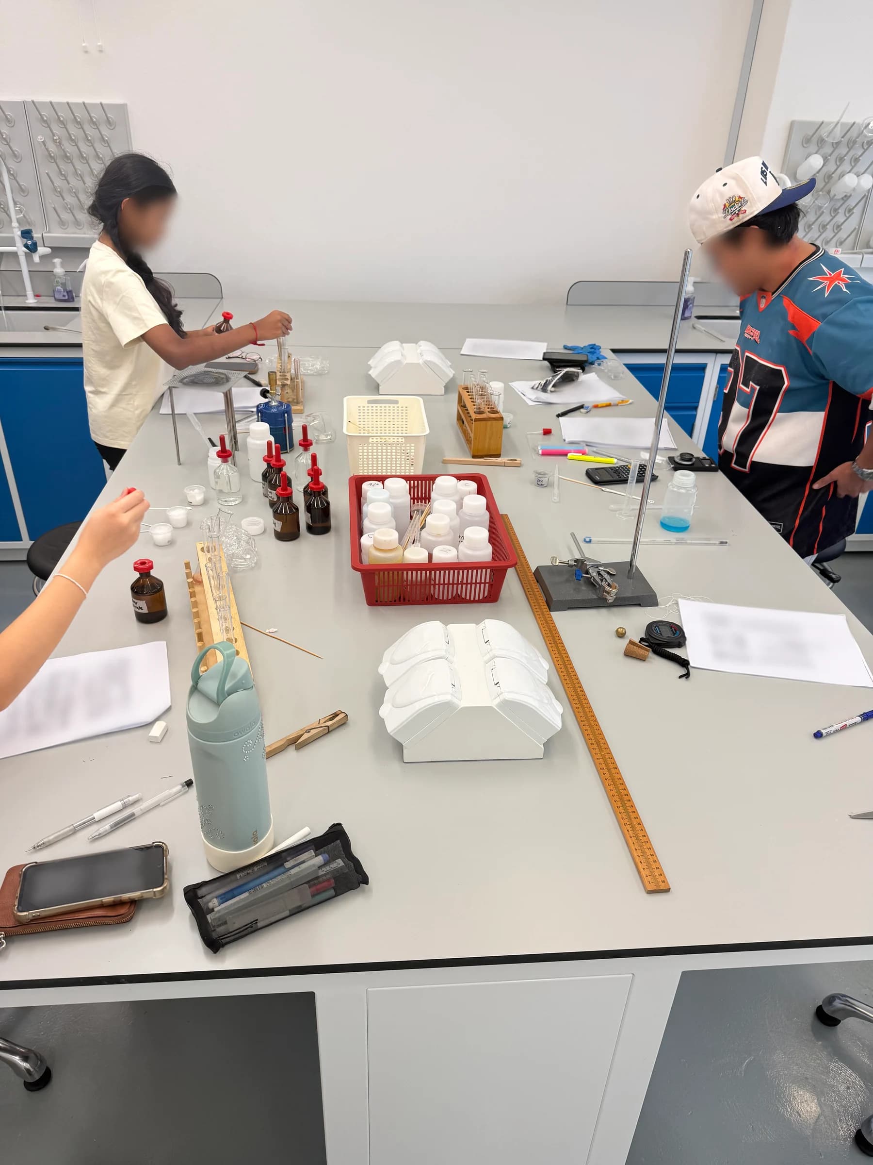Students handling reagents and apparatus across a shared bench during an Eclat Chemistry lab session