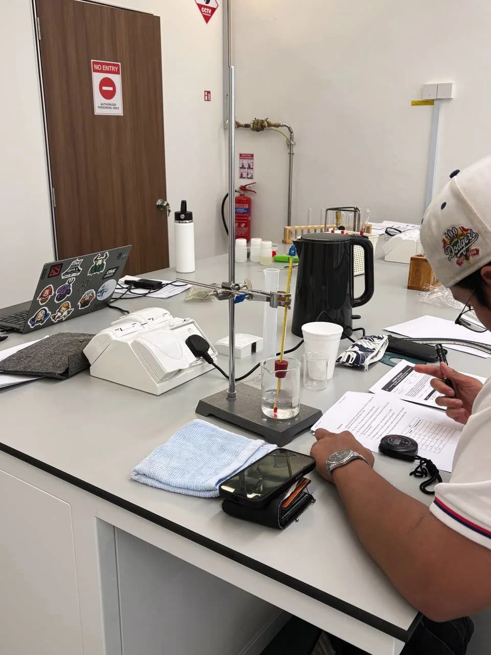 A student recording measurements beside a thermometer and beaker in an Eclat Physics practical