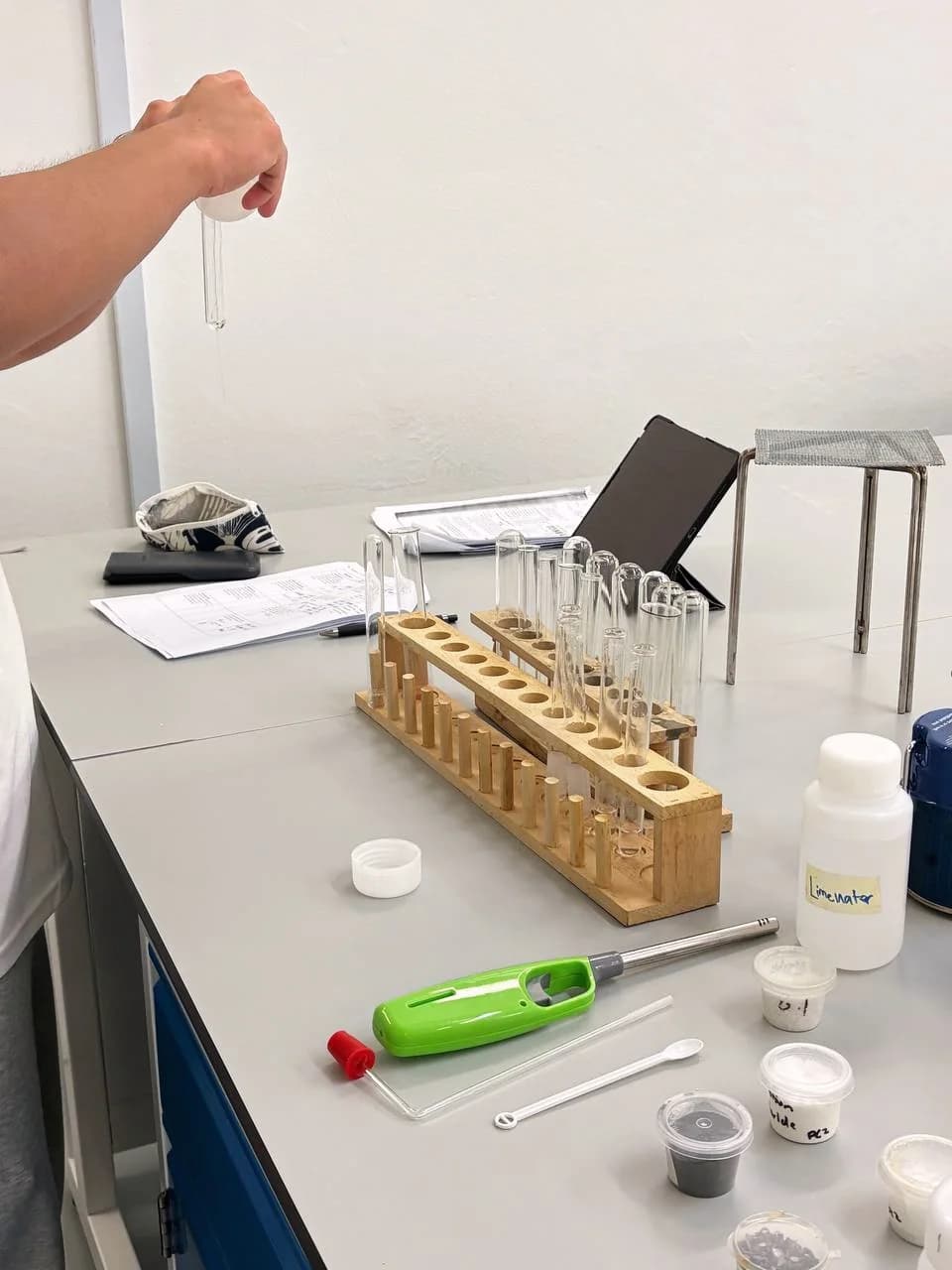 A hand holding a test tube above a rack during an Eclat Chemistry practical