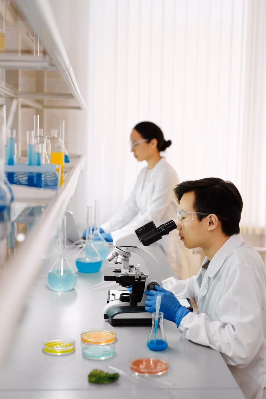 Two scientists working with microscopes and samples in a laboratory