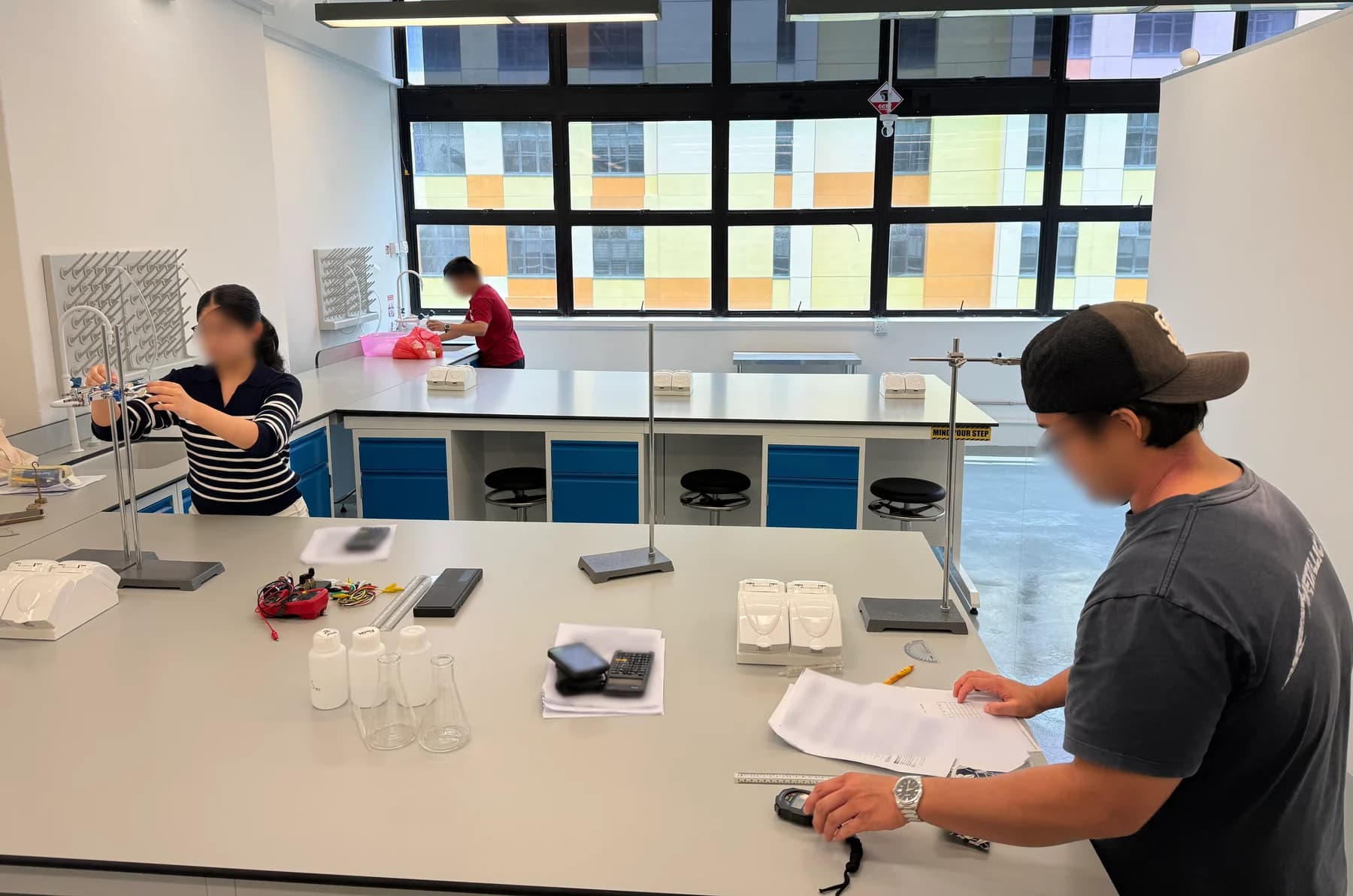 Students adjusting apparatus and recording measurements at shared laboratory benches during an Eclat session