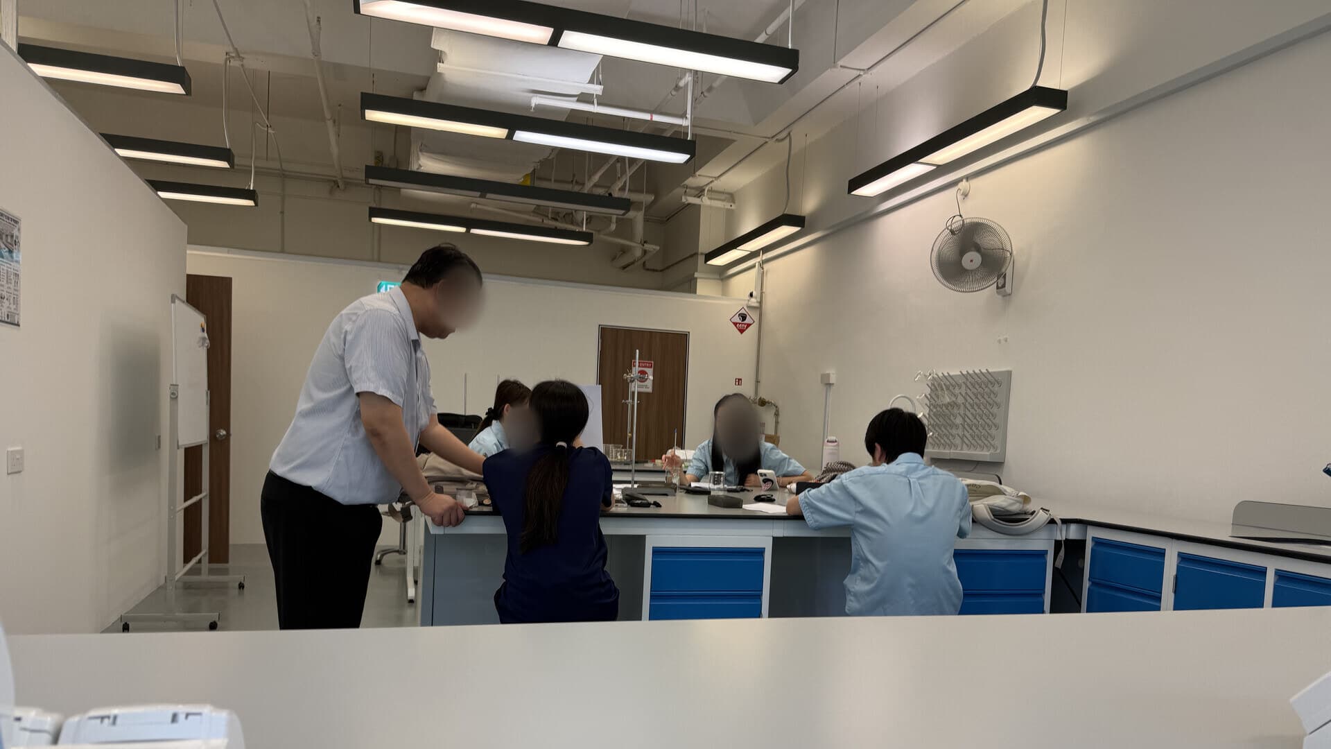 A tutor guiding students at the central bench in Eclat's Henderson practical laboratory